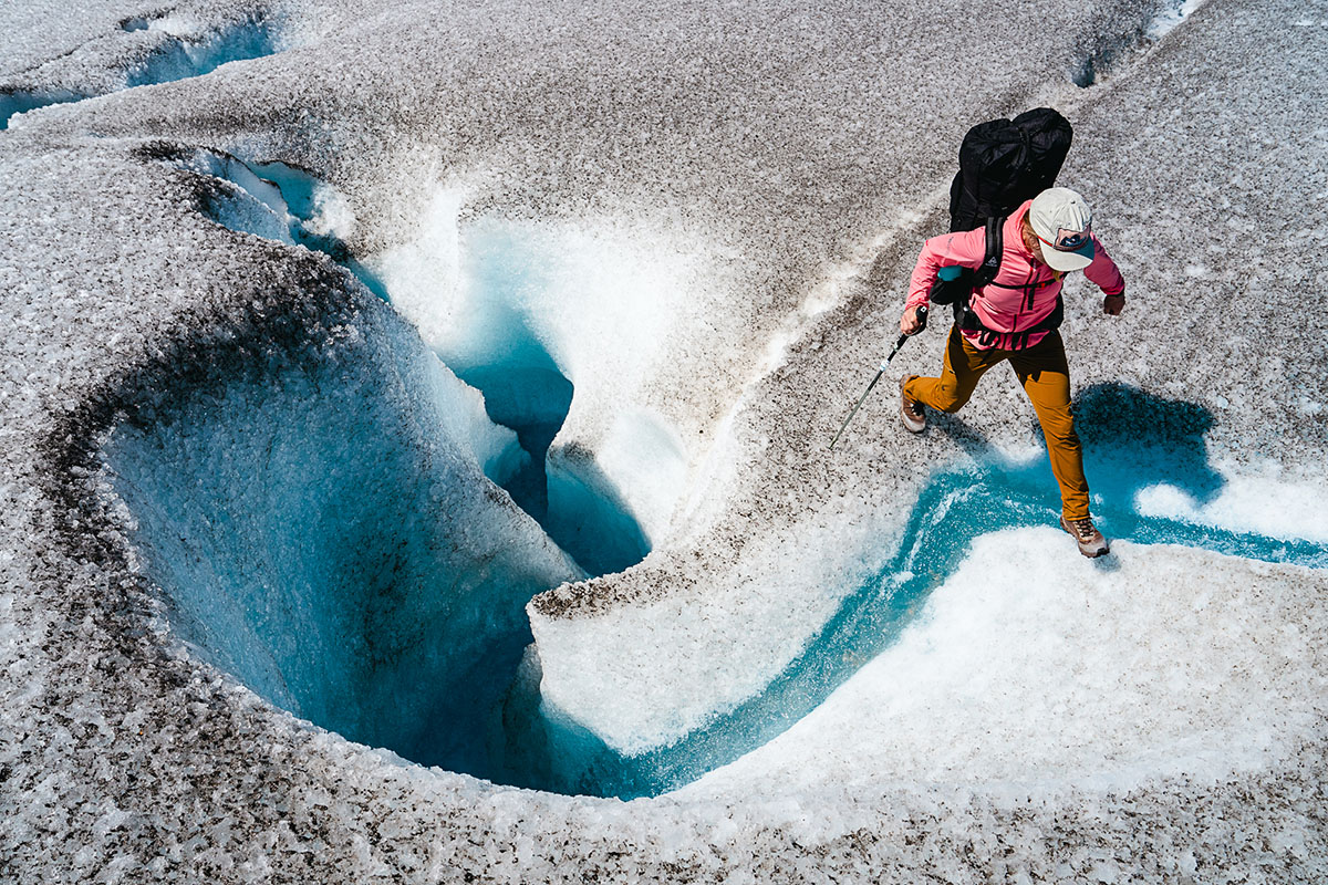 A woman hops over a tiny glacial rivulet while navigating wild, icy terrain.