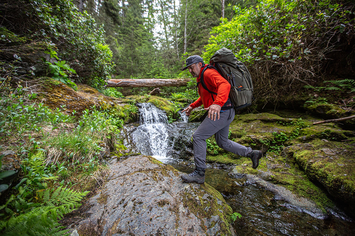 A man takes a leap from trail to rock as he crosses a rushing stream.