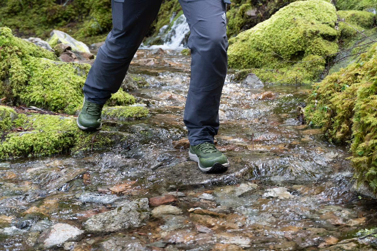 A hiker steps onto a slippery rock and navigates moss along the trail.