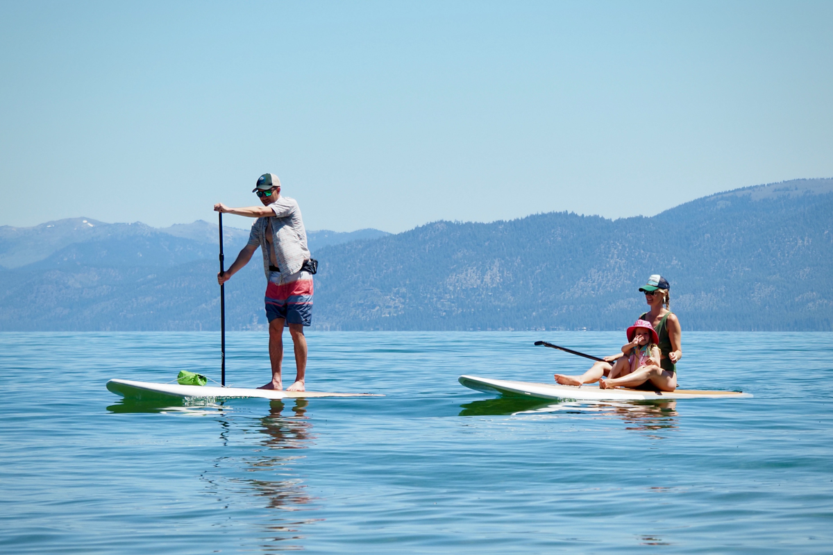 A family rides two paddle boards on a still lake