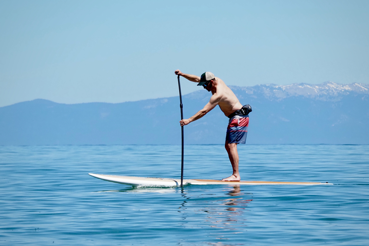 A man paddling a paddle board over still lake water