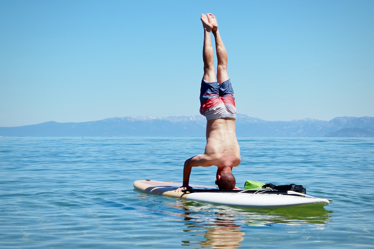 A man performing a headstand on a paddle board in a lake
