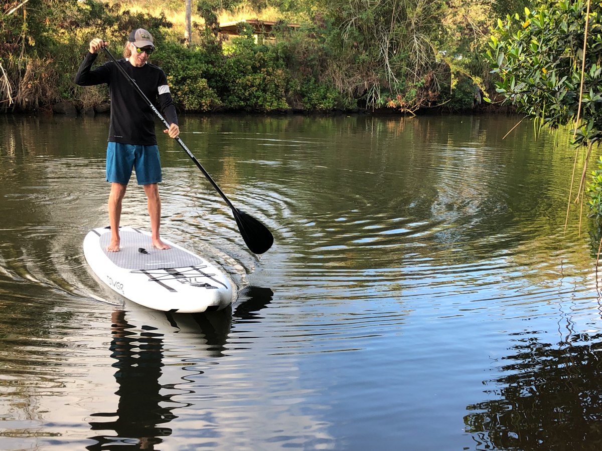 A person paddling on a black and white paddle board in still water