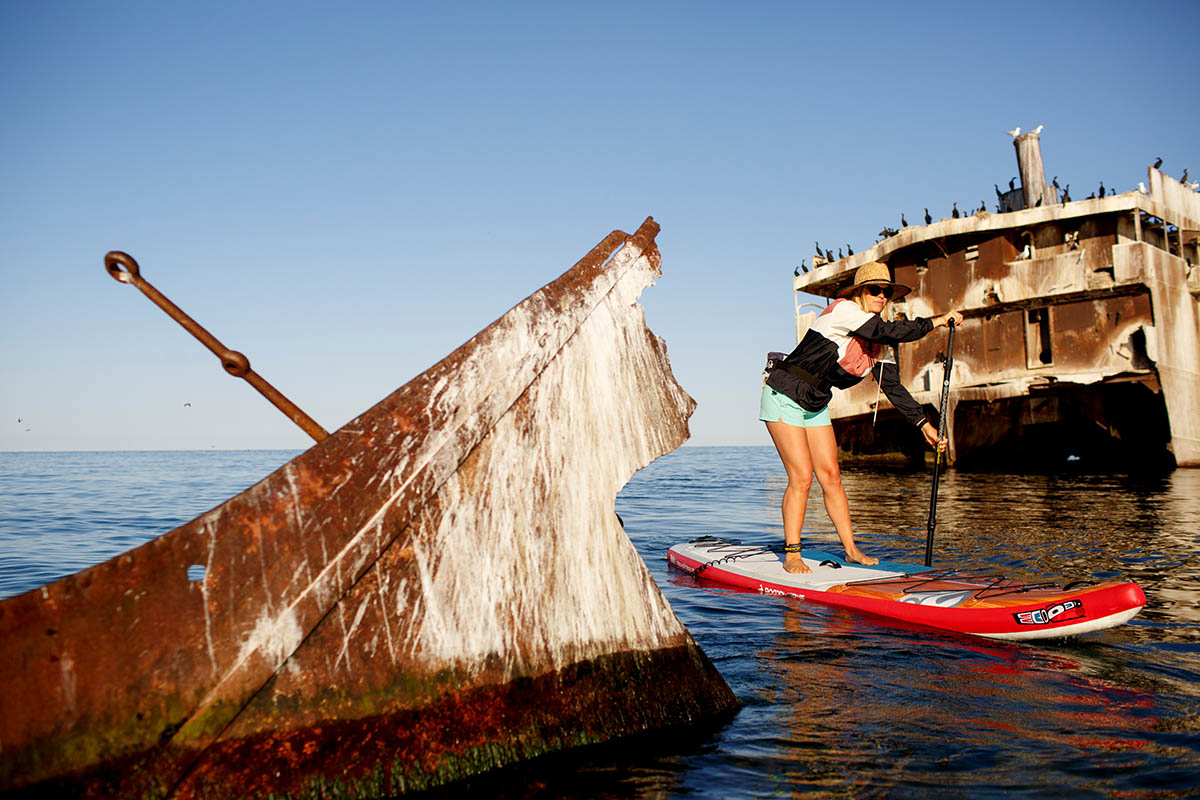 A woman paddles a SUP through ship wreckage on a lake.
