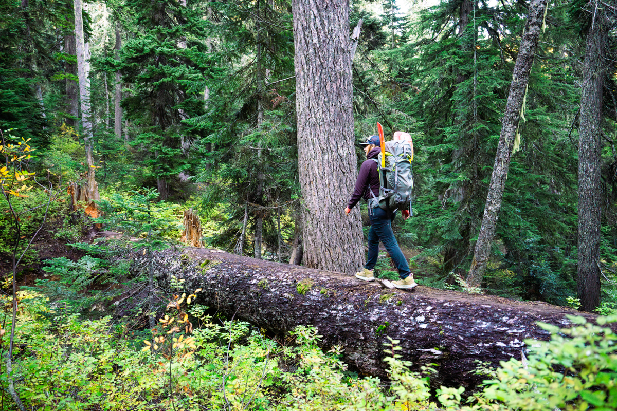 A woman hiking with a backpack over a fallen log