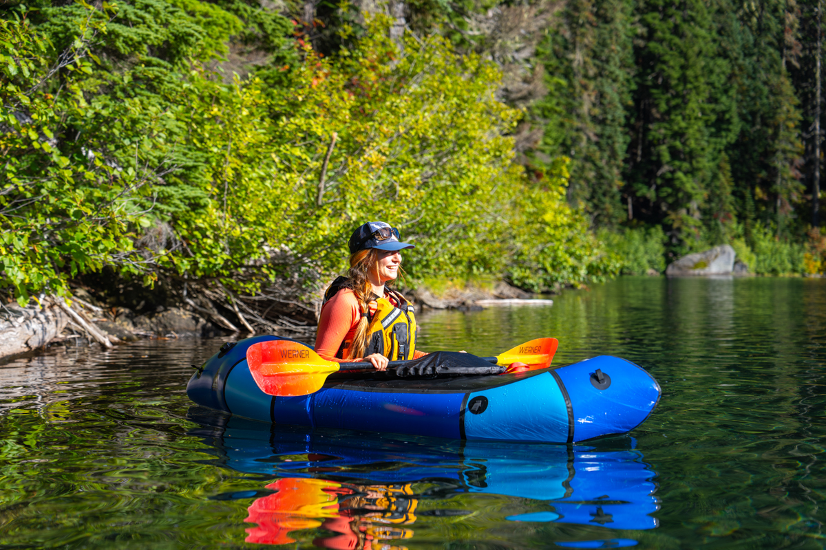 A woman sitting in a blue packraft in the water with a paddle in hand