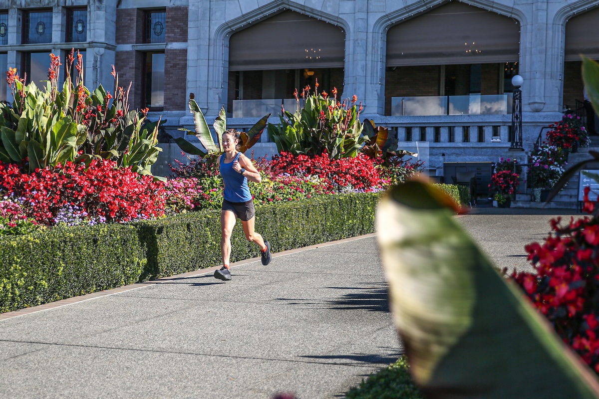 A woman runs in front of a stone building in a pair of Hoka Bondi shoes 