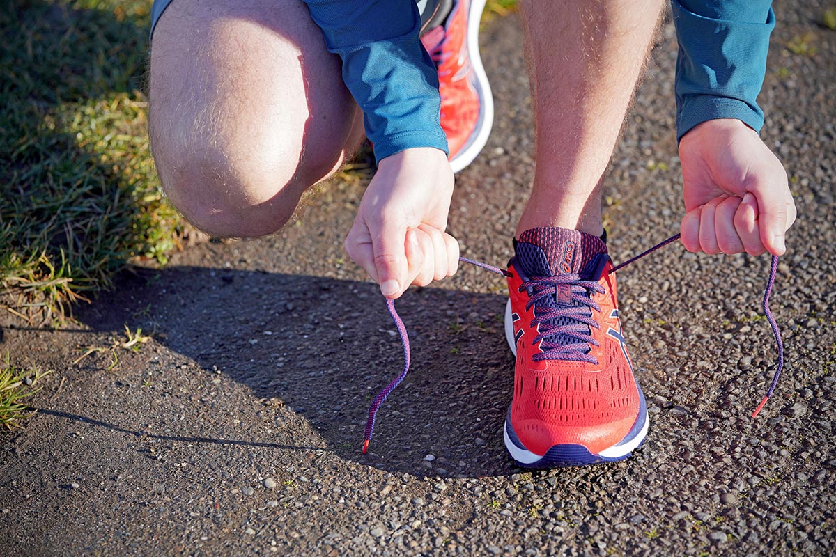 A woman laces up running shoes in a bright color 