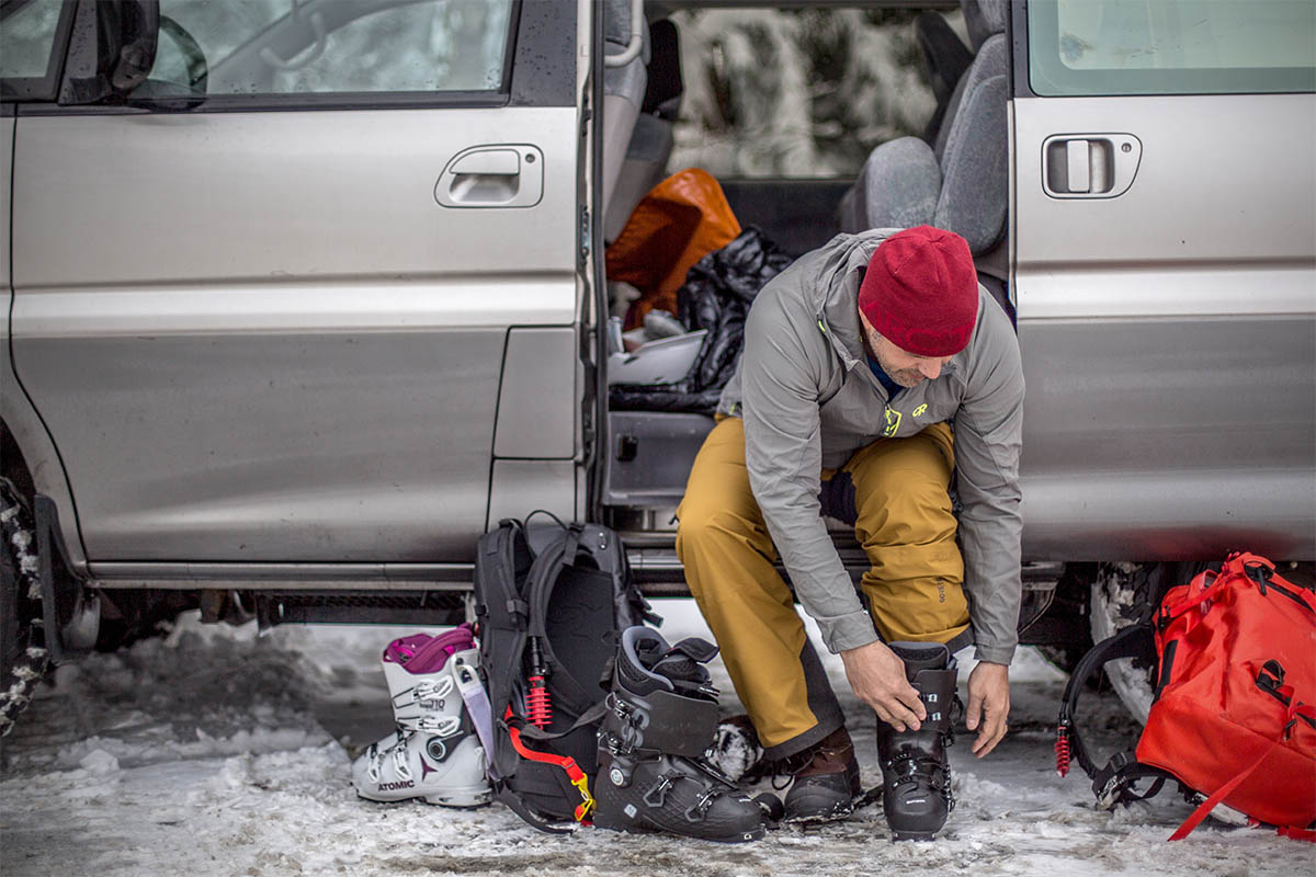 A man sits in the open door of a van to buckle up his ski boots