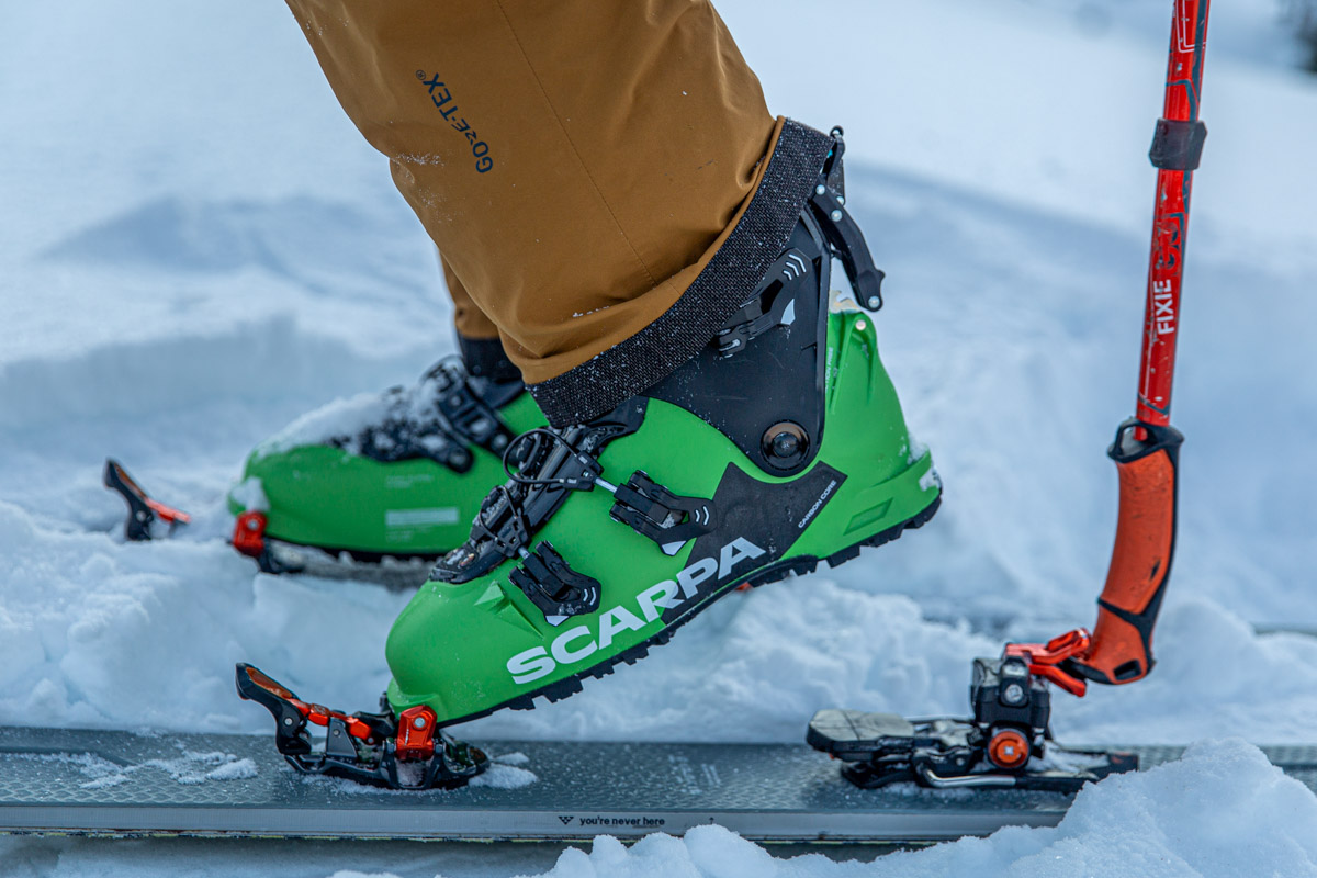 A close up of a green pair of Scarpa ski boots attached to touring bindings