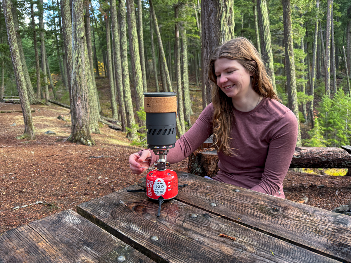 A woman boiling water while camping, wearing the REI Midweight Long-Sleeve
