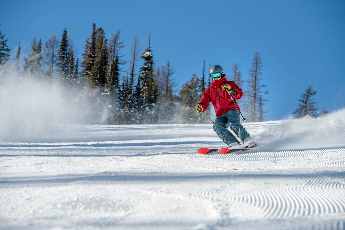 A man in a red ski jacket skiing down a newly groomed trail