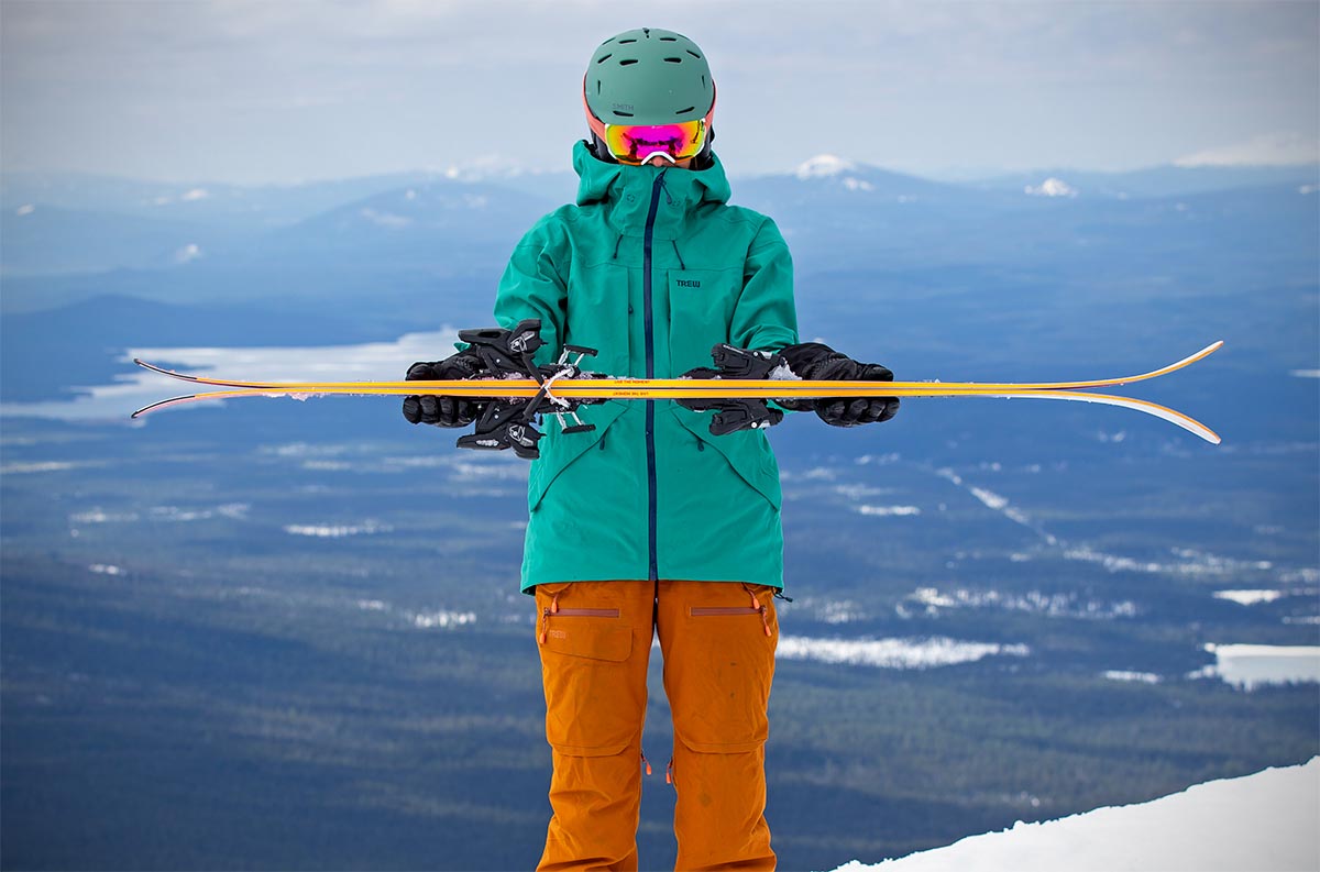 A skier holds up a pair of skis base to base to show the rocker and camber profile