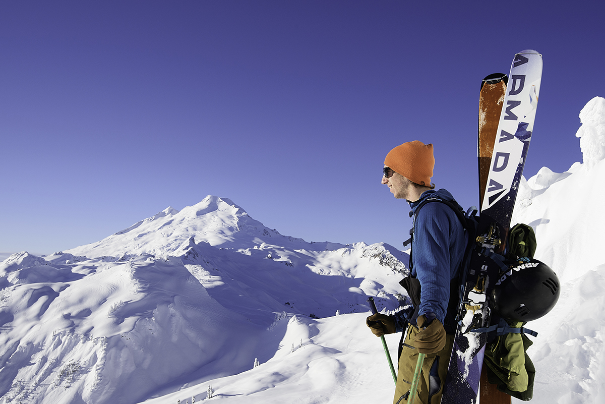 A man carries a pair of Armada skis on his backpack.