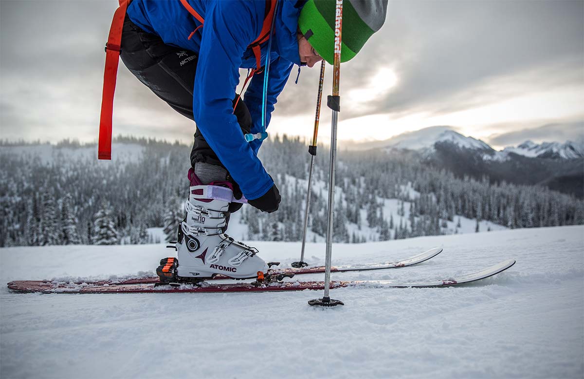 A woman bends over to buckle her Atomic Hawk Ultra XTD 110 ski boots.