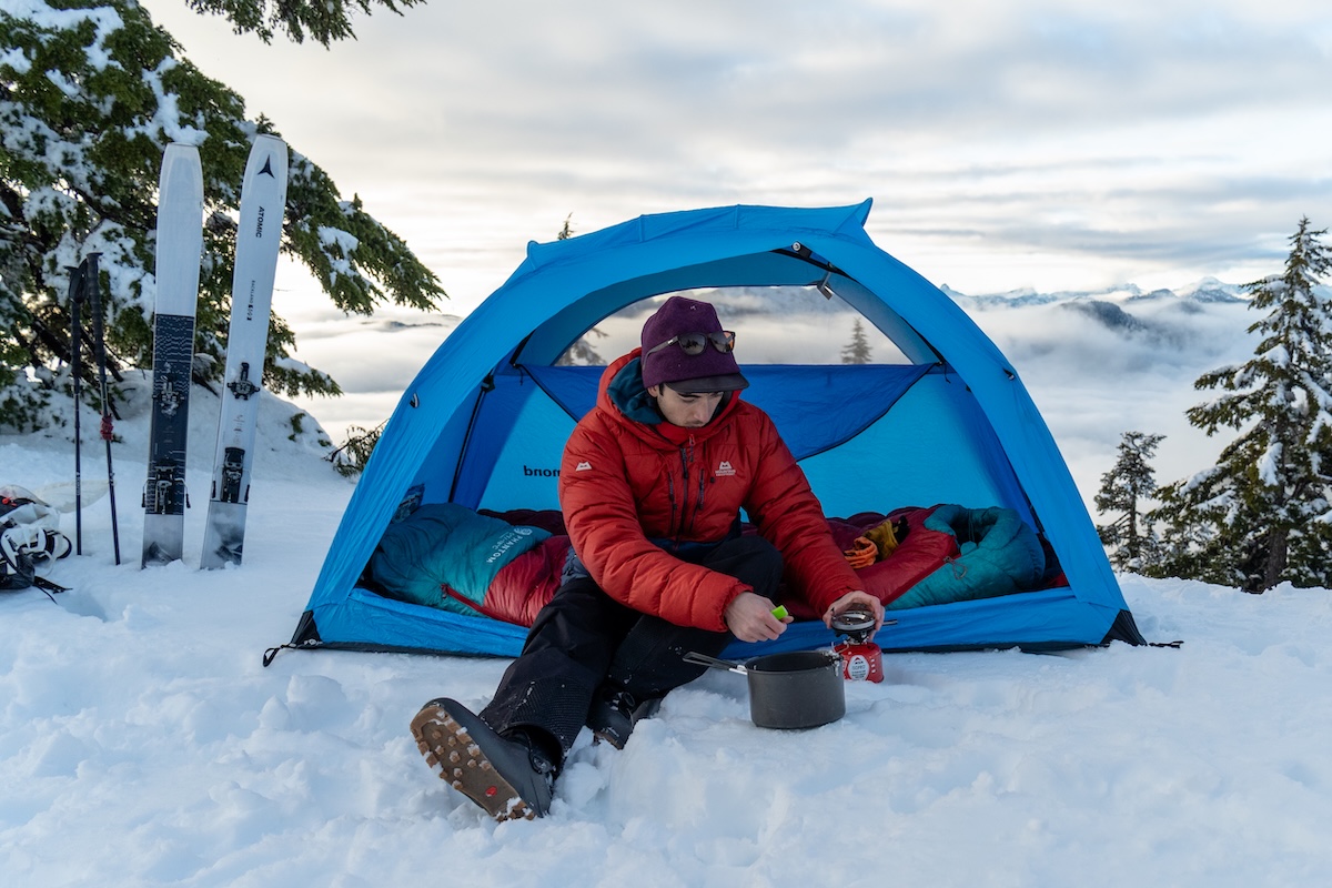 A man sits in a tent while testing down jackets on a ski trip