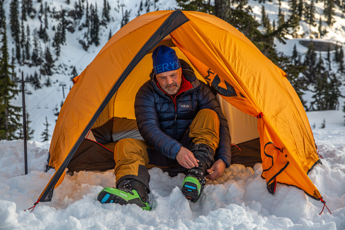 A man sitting in a tent and pulling on ski boots