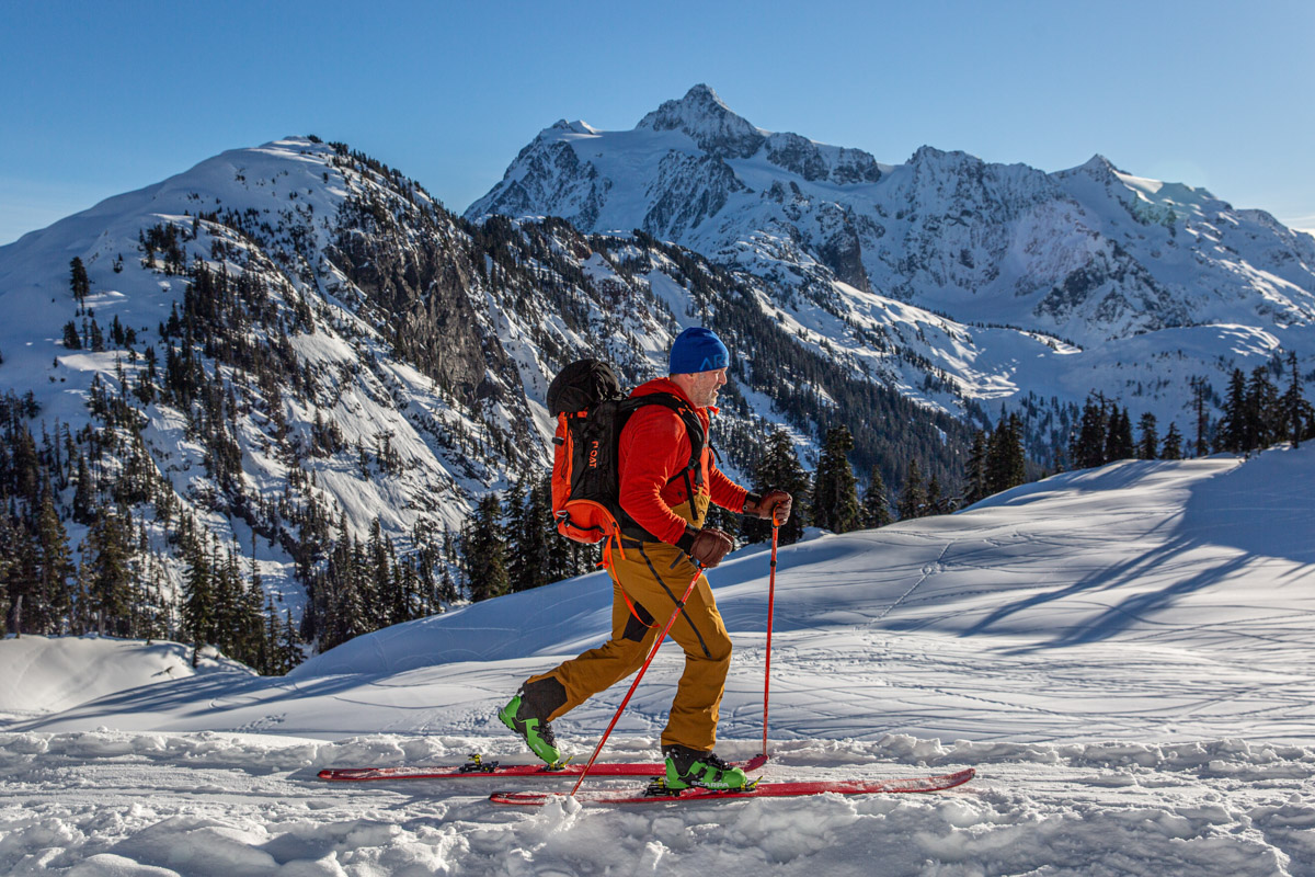 A man skiing across the snow with a mountainous background