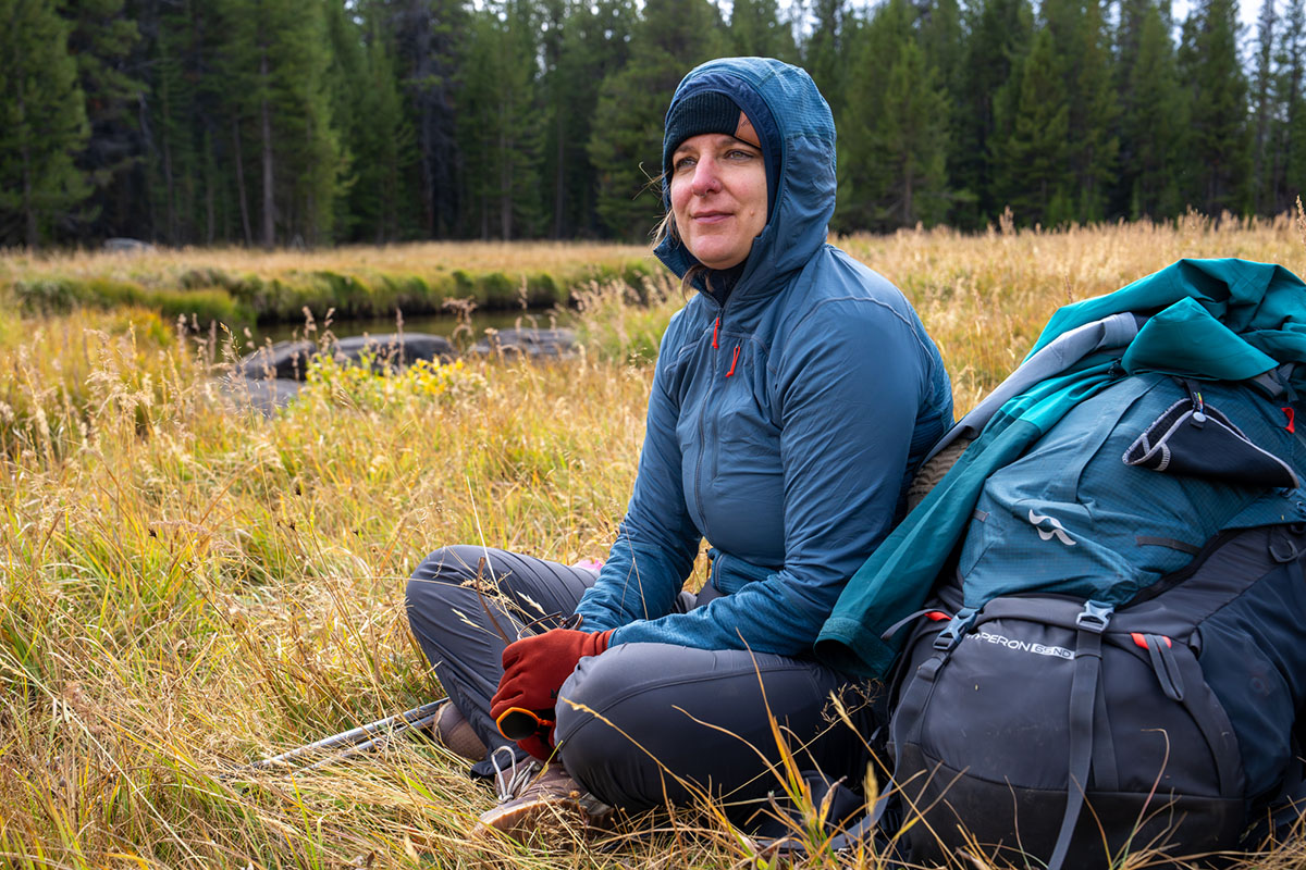 A woman sits next to a backpack in a field