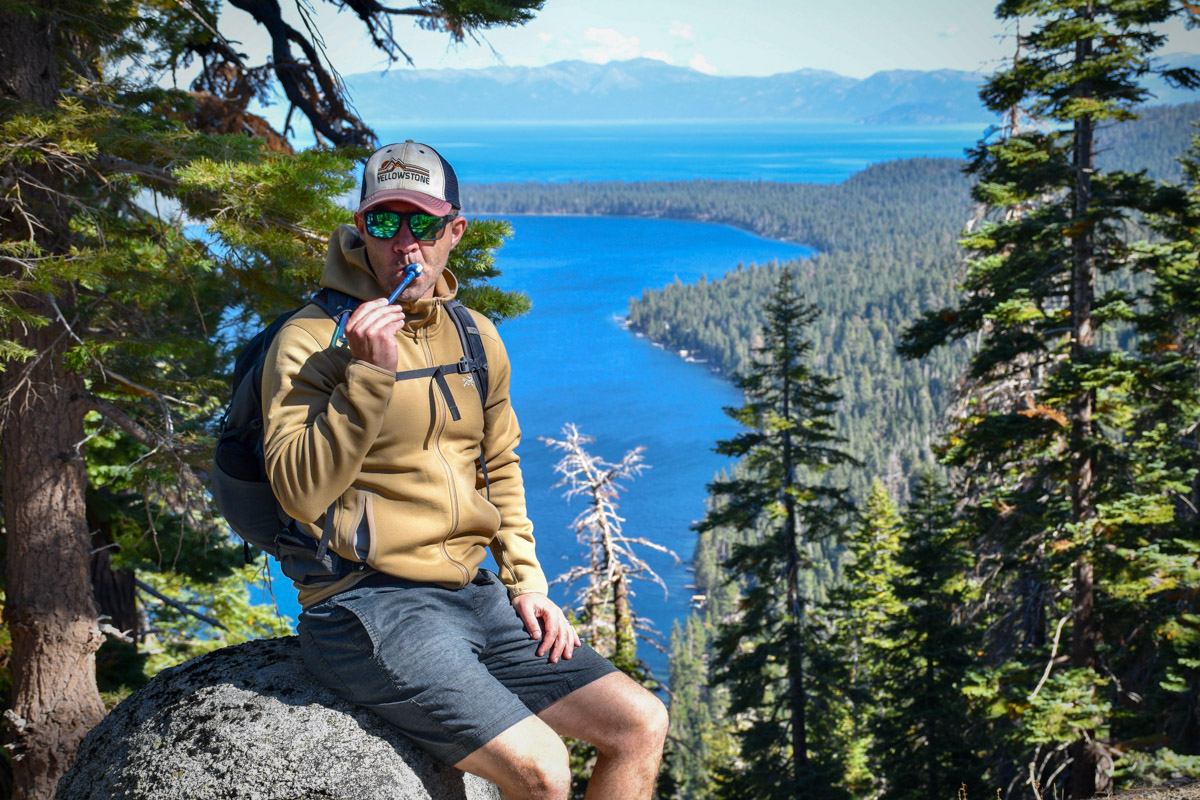 A man in a fleece jacket stops to drink water with Lake Tahoe in the background