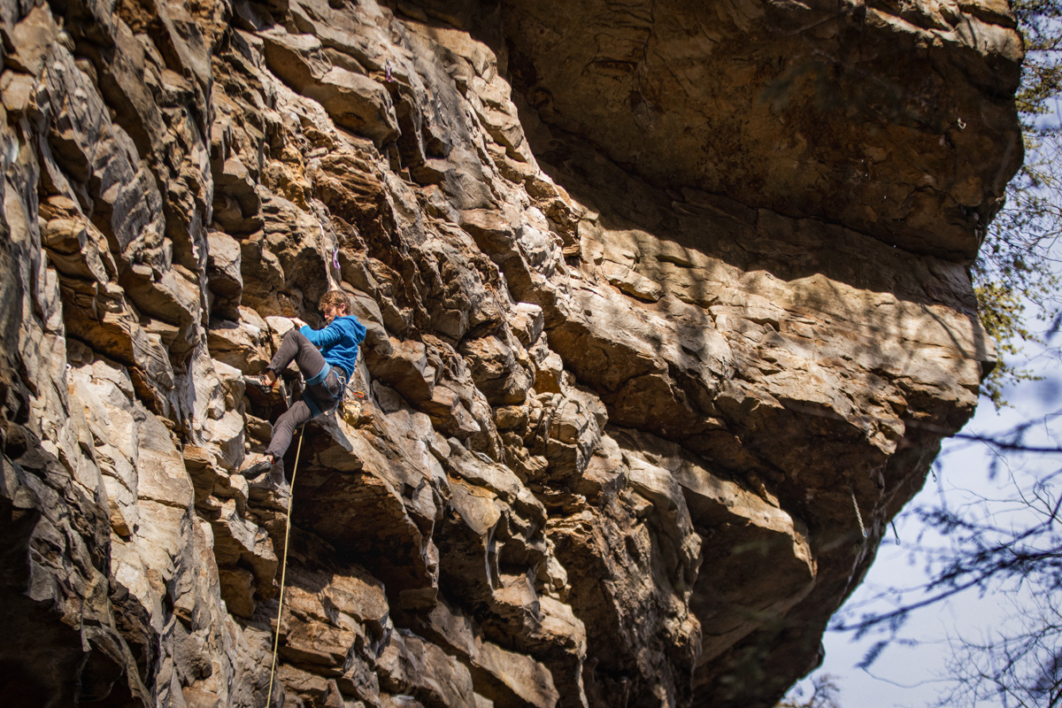 A man in a blue fleece jacket sport climbs on a sunny day