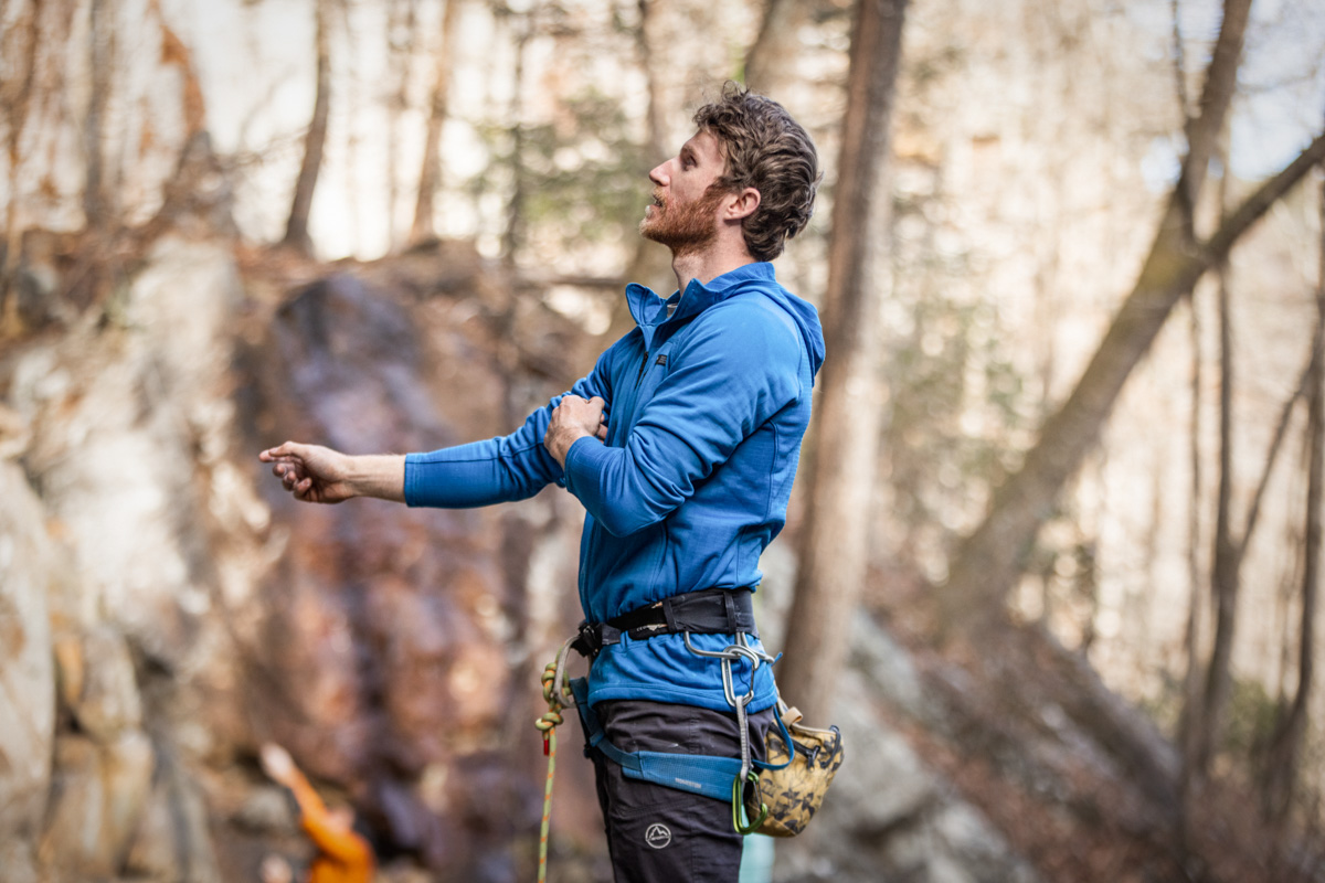 A male rock climber adjusts his fleece jacket while assessing his climb.