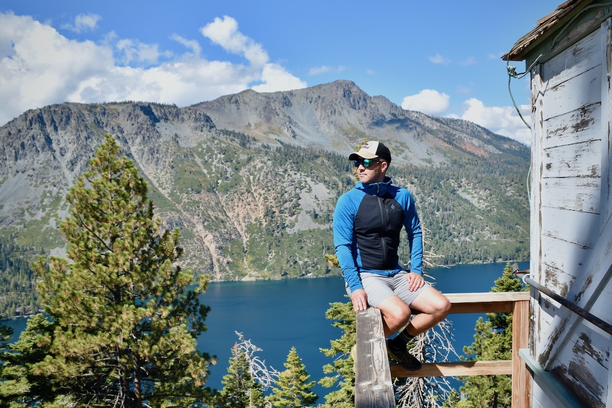 A man sits on the railing of a fire lookout with a lake in the background