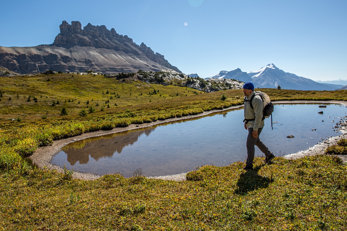 A man surrounded by mountains walks around a small pond
