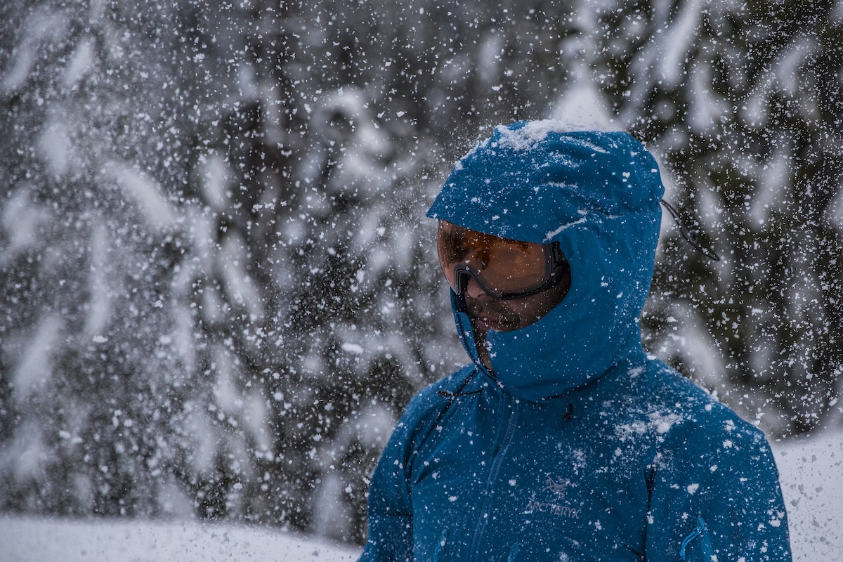 A man stands in a heavy snowstorm with a hardshell jacket on