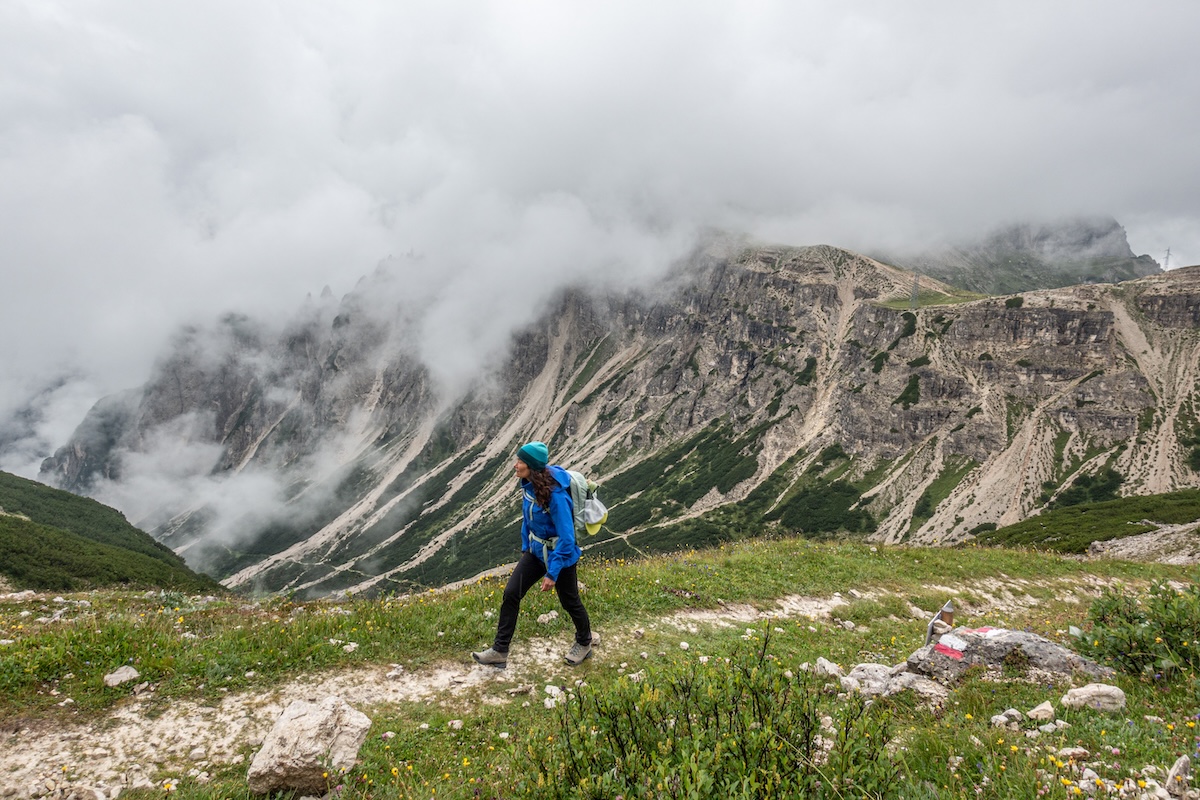 A woman hikes in front of a mountain with a hardshell jacket