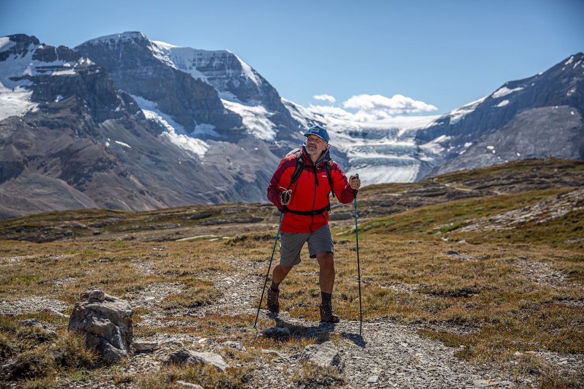 A man hikes through a valley with trekking poles and mountains in the background
