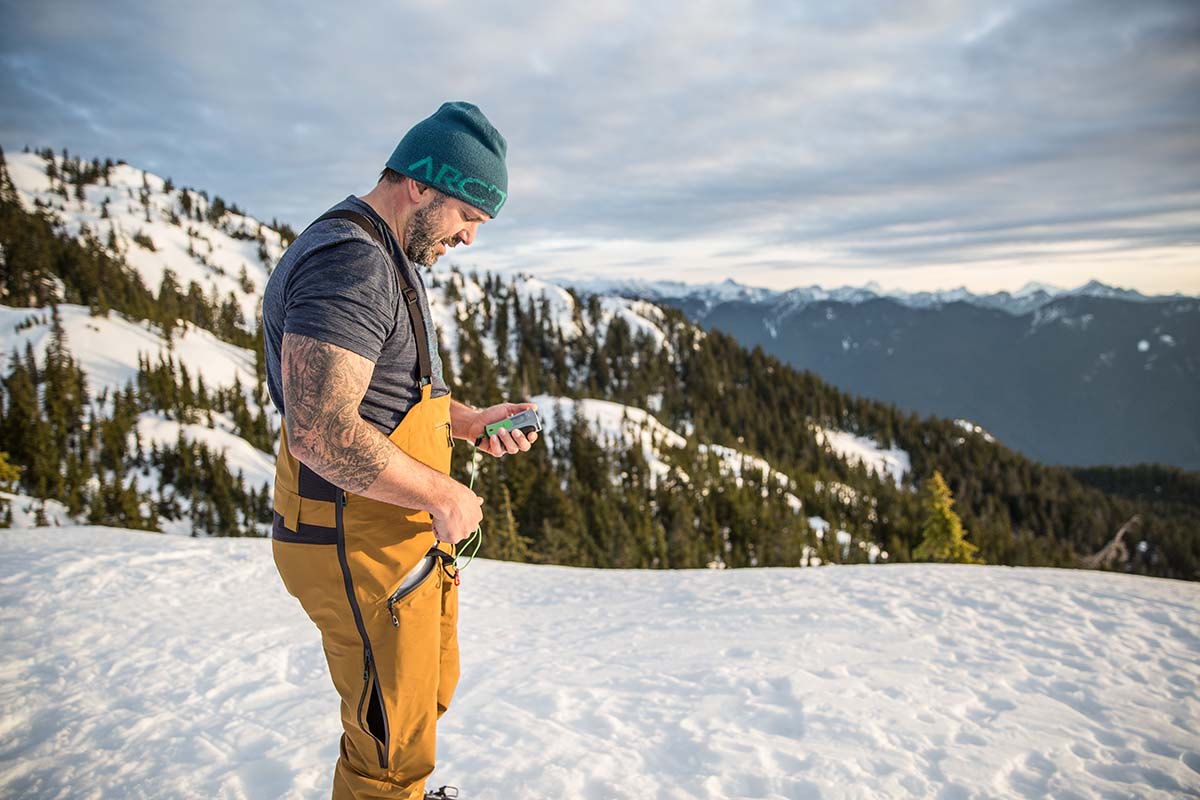 A man in yellow bibs removes an avalanche beacon from his pocket