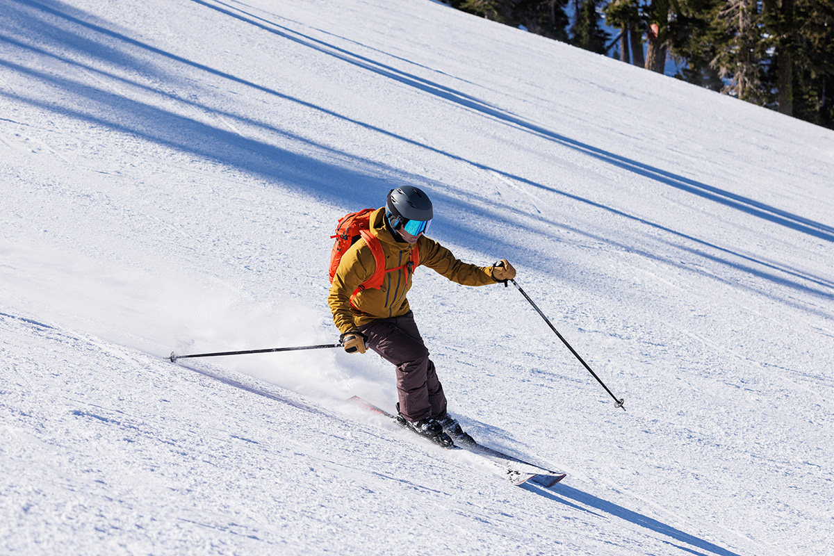 A man with a backpack skiing a groomer in the REI Powderbound Insulated pants