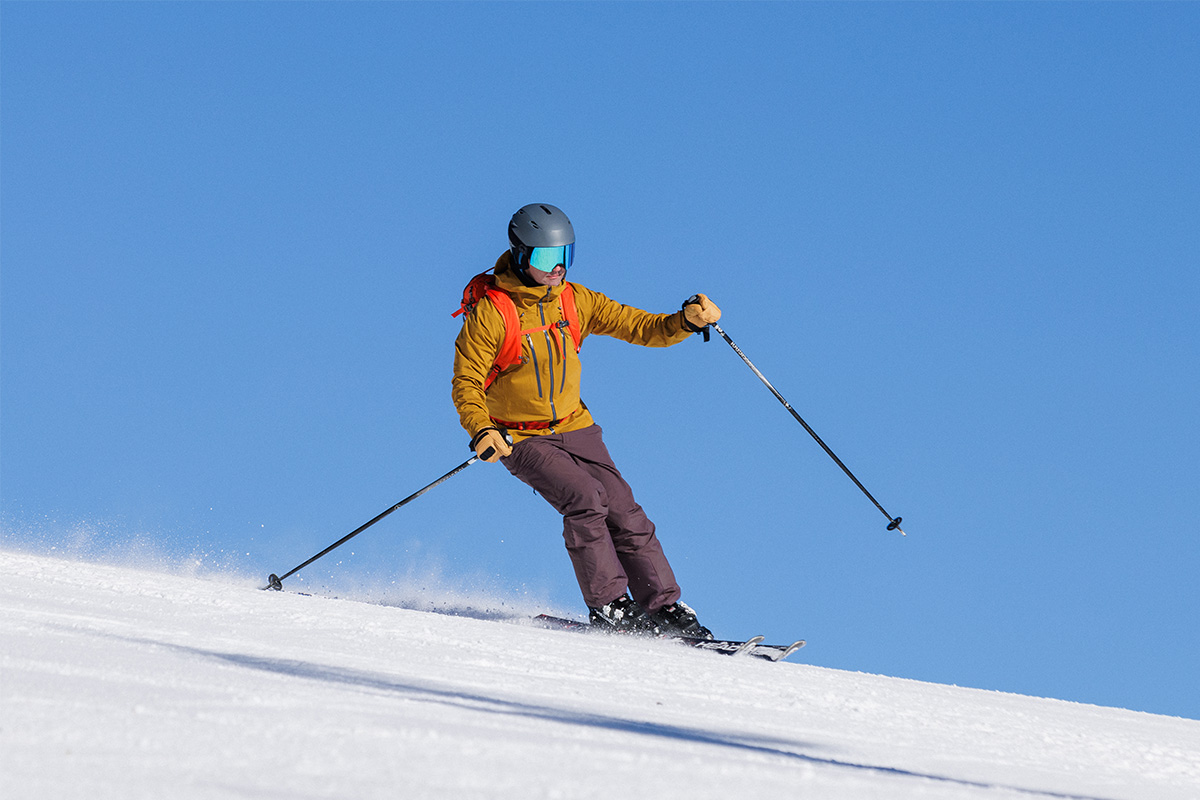 A man skis a groomer in the REI Powderbound pant with a clear blue sky behind him