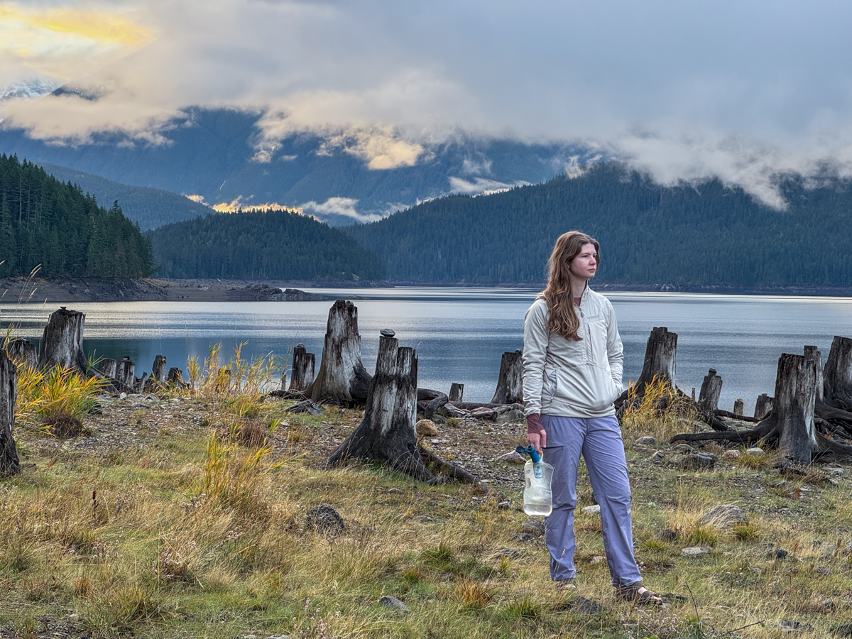 A hiker poses in front of an alpine lake at sunset.