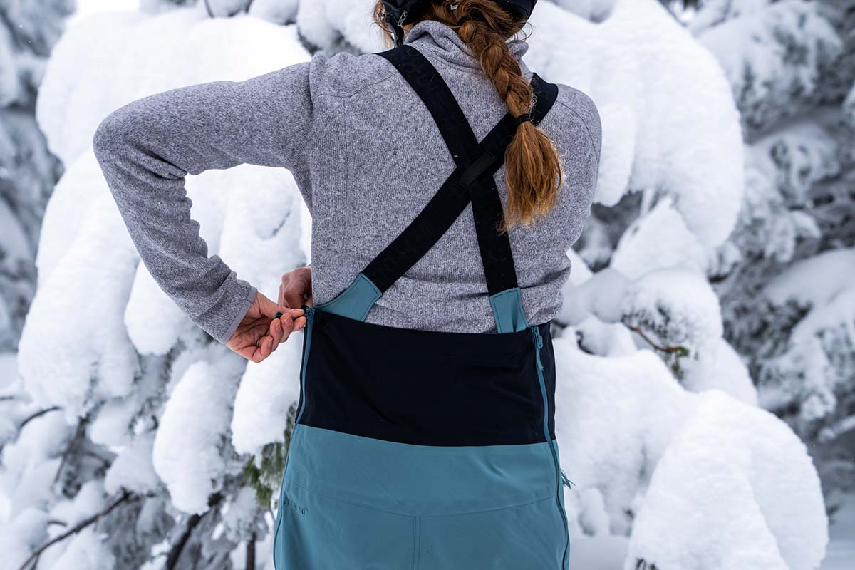 A woman zips her snowboard bibs over her fleece layer.