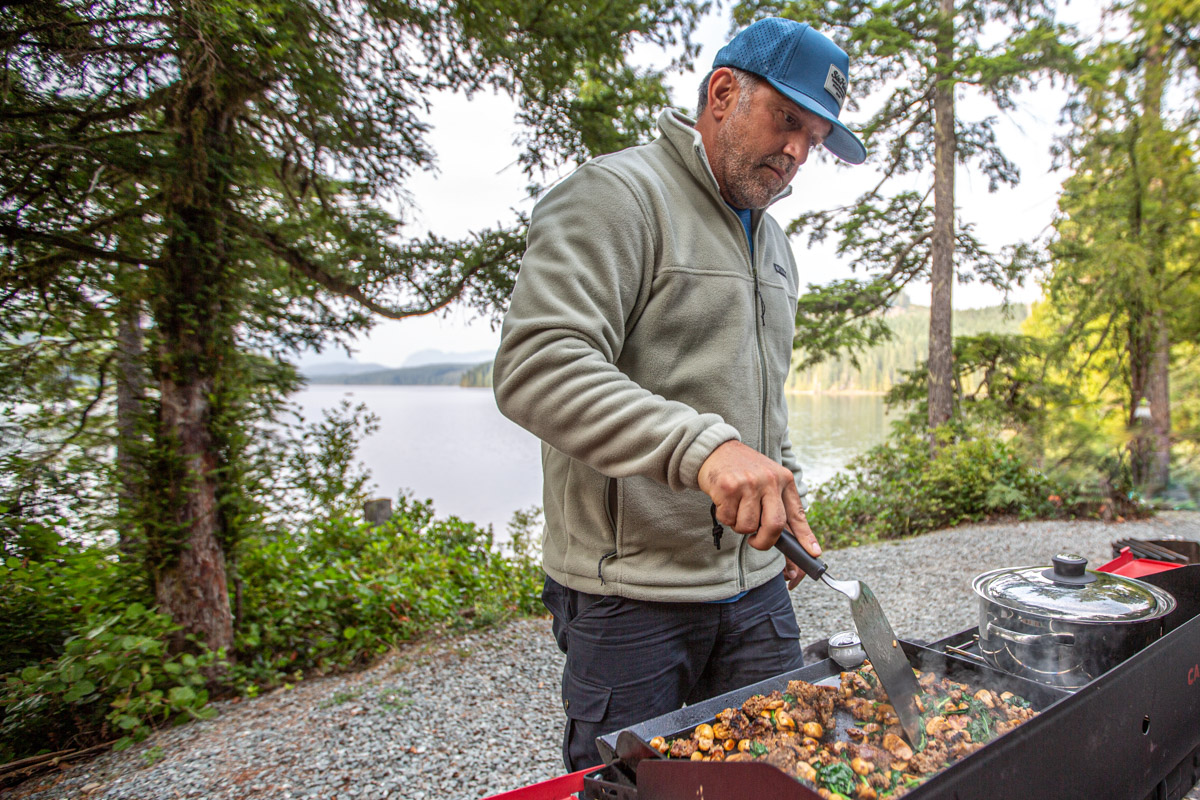 A man cooking food on a camp stove wearing a fleece midlayer