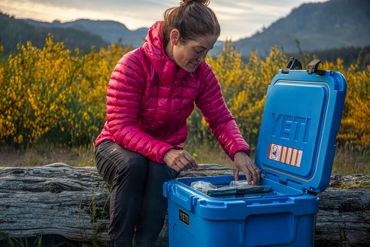 A woman sorting through a cooler wearing a pink midlayer