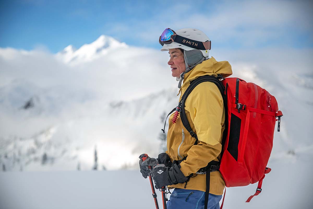A woman standing high up in the mountains wearing a ski backpack