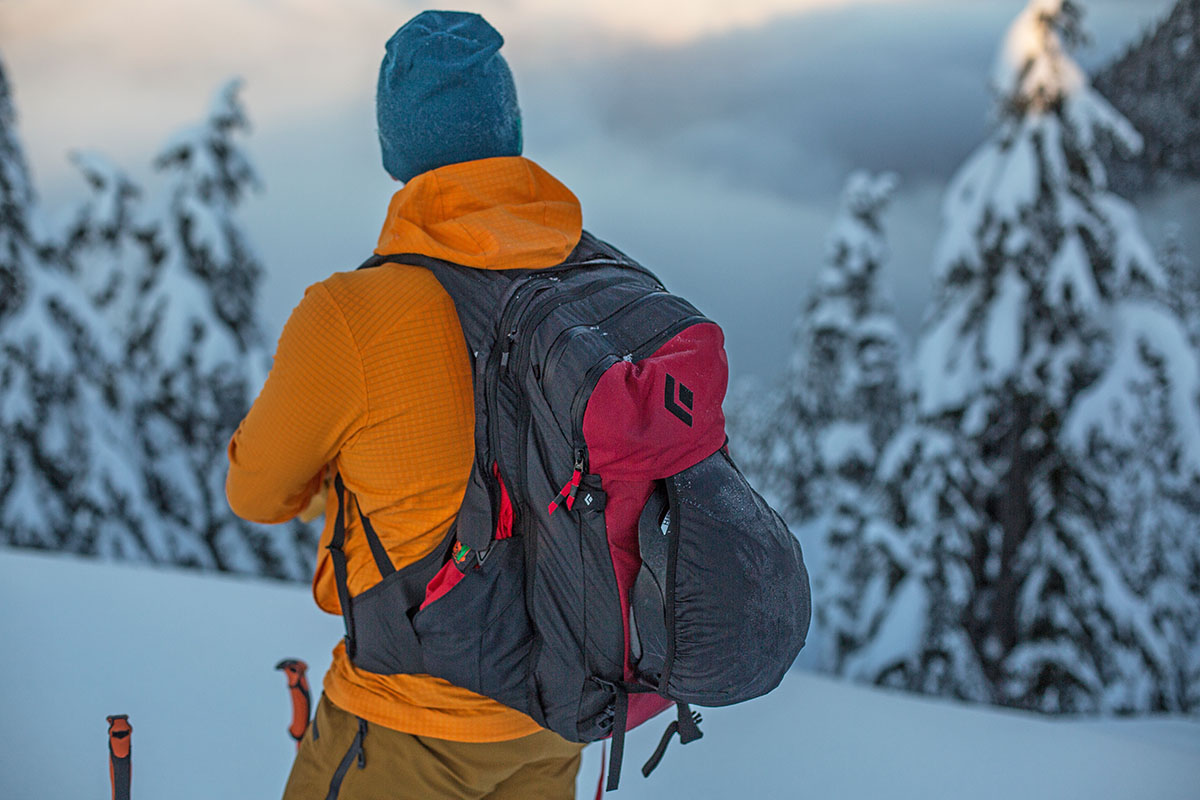 A man looking at the snowy sunset, showing off the helmet carrier on a Black Diamond backpack