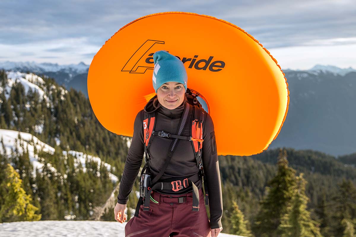 A woman wearing an inflated avalanche airbag with mountains in the background