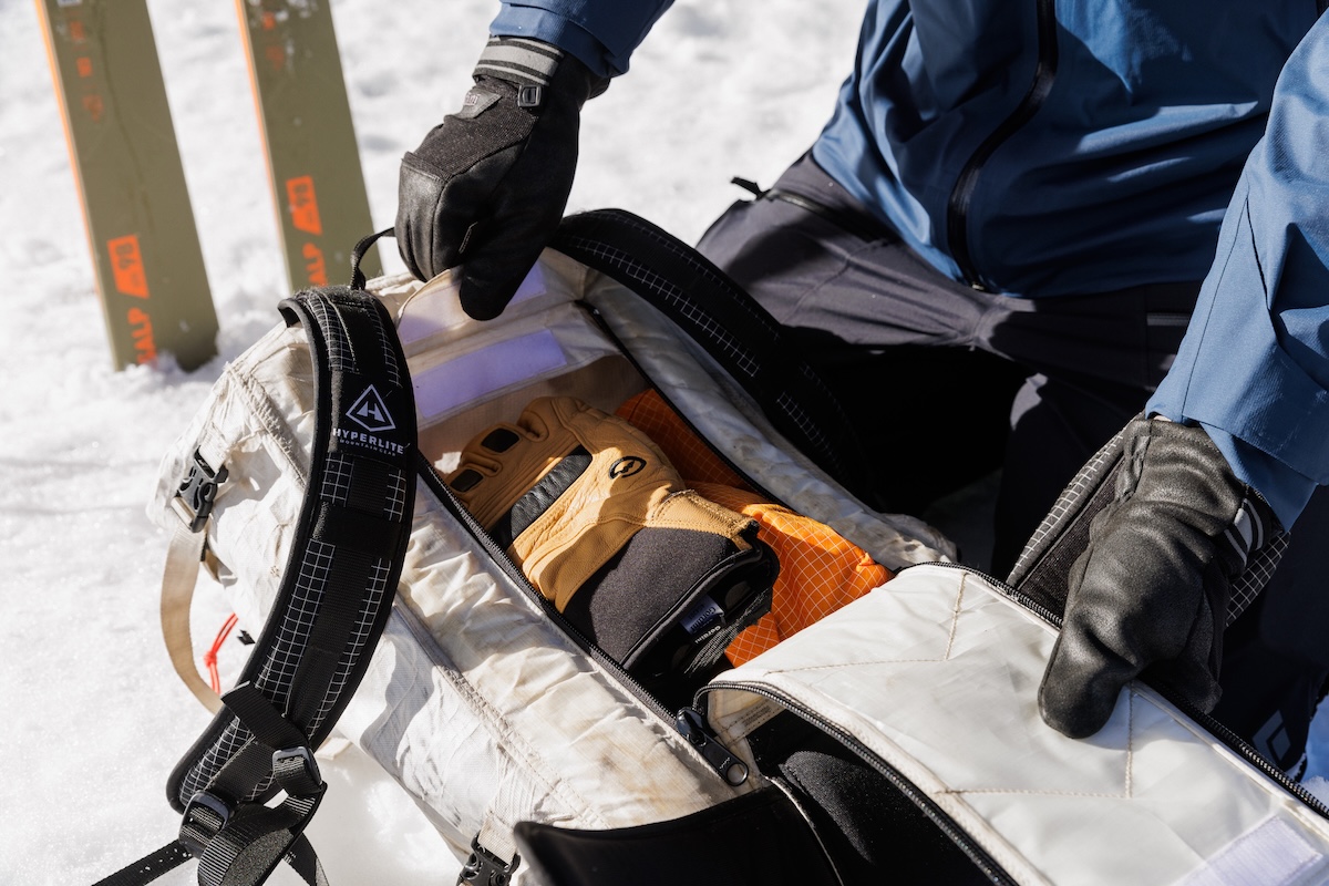 A ski backpack open on the snow showing off the interior contents