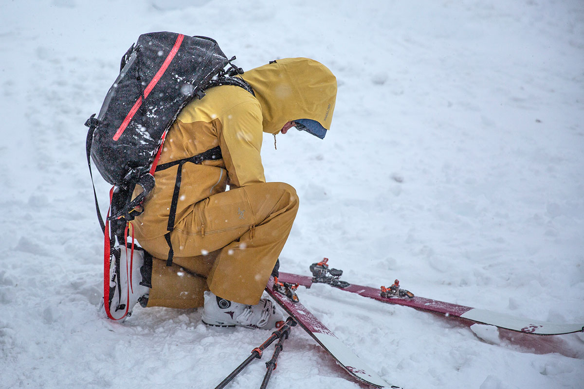 A woman crouched in the snow adjusting skis wearing yellow ski bibs