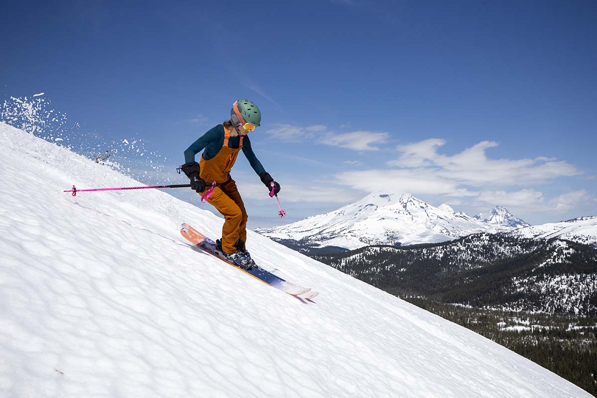 A woman wearing orange ski bibs skiing at Mt Bachelor Ski Area