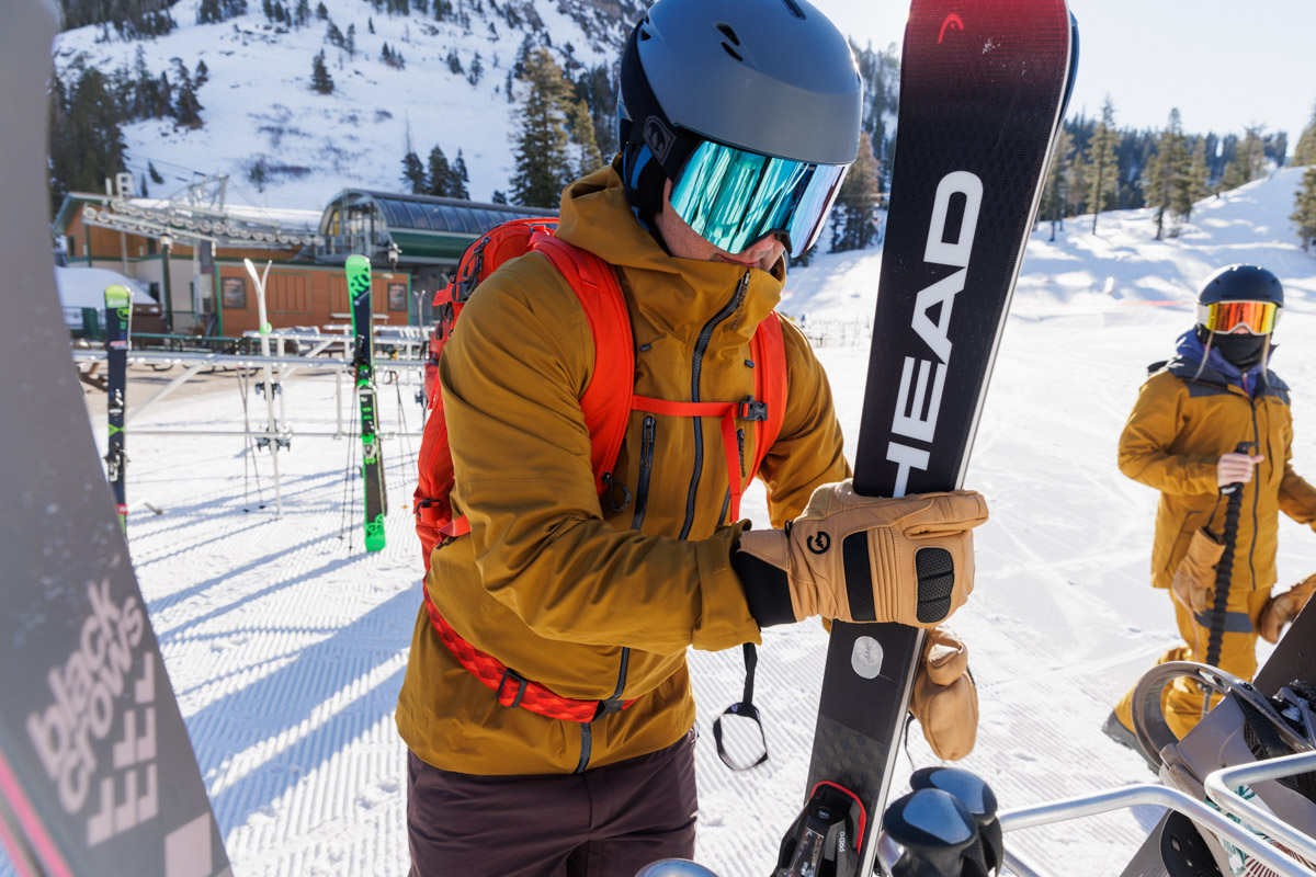 A skier wearing 3-fingered gloves places his skis in a rack at the resort