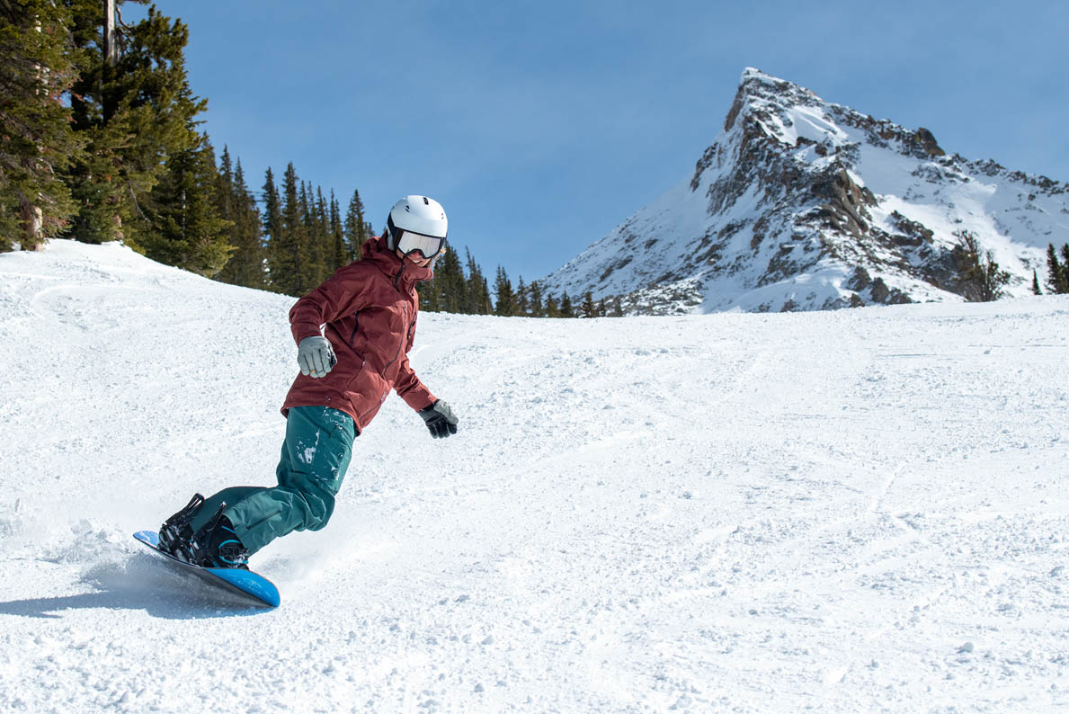 A smiling woman snowboards down a slope in bright light