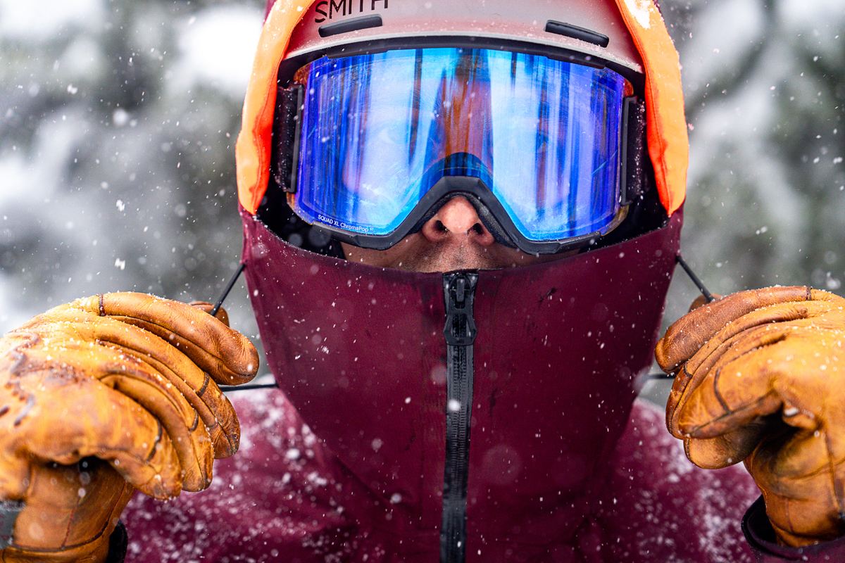 A man pulls his hood tight over goggles in snowy weather