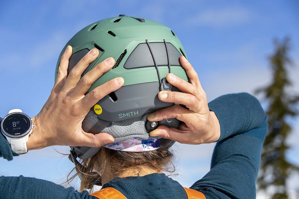 A woman adjusting the back of her ski helmet