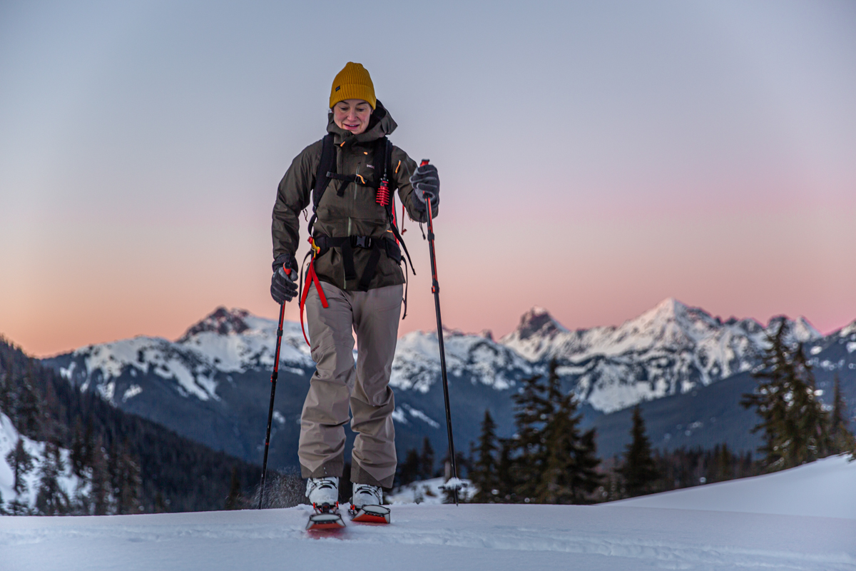 A woman is shown skinning up a snowy hill at sunrise