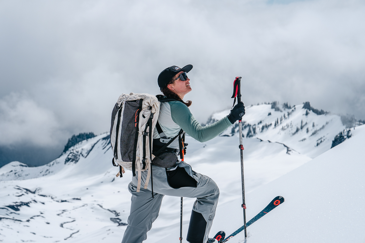 A woman ski touring in the mountains looks off into the view uphill